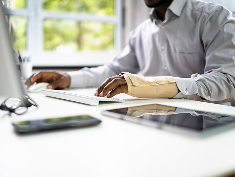 A man with a wrist cast sitting at a desk using a laptop - Legal Advantage Group