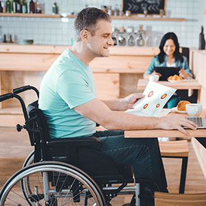 A person in a wheelchair works on a laptop, with another person in the background.